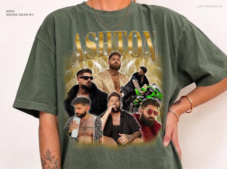 May include: A moss green t-shirt featuring the name ASHTON in gold lettering at the top. The graphic includes multiple photos of a bearded man in various outfits and poses, including one on a green motorcycle, set against a gold lightning background.
