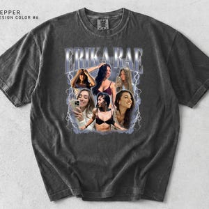 May include: Pepper-colored t-shirt with a distressed look. The front features a graphic of the name "ERIKA RAE" in a stylized font, surrounded by images of women. The design includes lightning bolt accents.