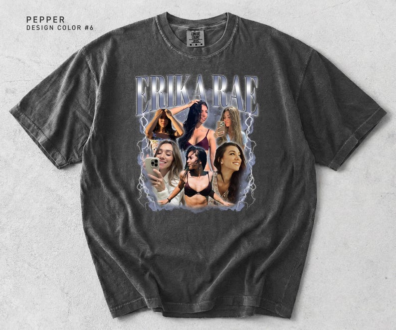 May include: Pepper-colored t-shirt with a distressed look. The front features a graphic of the name "ERIKA RAE" in a stylized font, surrounded by images of women. The design includes lightning bolt accents.