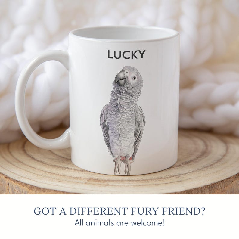 May include: White ceramic mug featuring a detailed illustration of a gray parrot with the word "LUCKY" above it. The mug also has the text "GOT A DIFFERENT FURY FRIEND? All animals are welcome!"