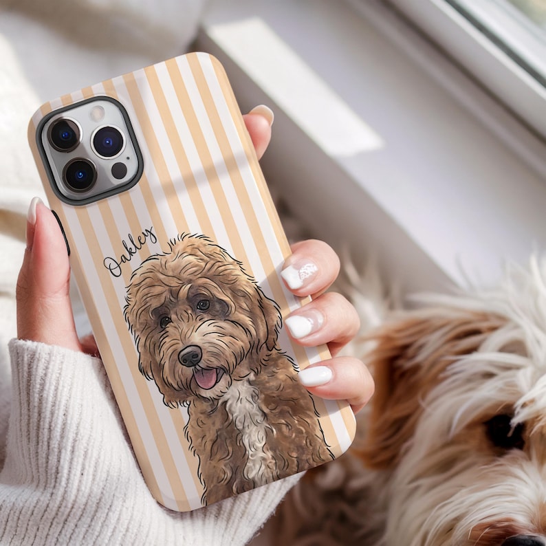 May include: A phone case featuring a light orange and white vertical striped background with a detailed illustration of a brown curly-haired dog. The name Oakley is printed in black script text next to the dog illustration on the phone case.