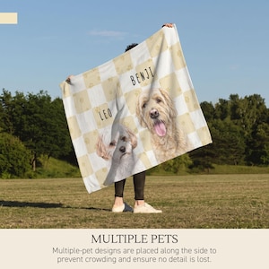 May include: A cream and white checkered blanket featuring illustrations of two dogs. The dog on the left is labeled with the name LEO, and the dog on the right is labeled with the name BENJI. Small paw print patterns are visible within the squares.
