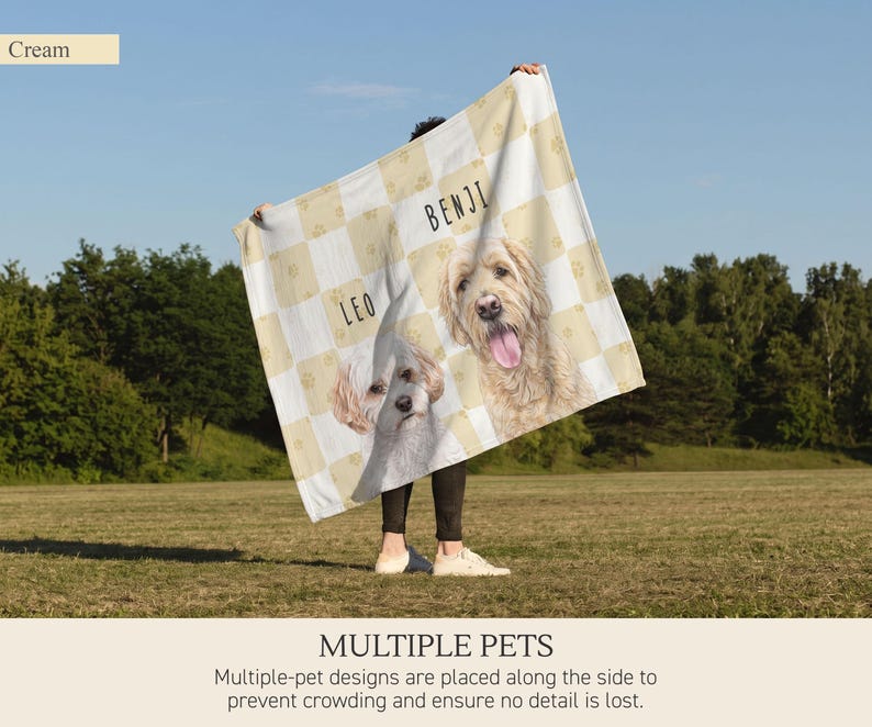 May include: A cream and white checkered blanket featuring illustrations of two dogs. The dog on the left is labeled with the name LEO, and the dog on the right is labeled with the name BENJI. Small paw print patterns are visible within the squares.