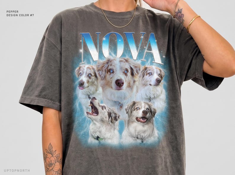 May include: A charcoal gray short-sleeve t-shirt featuring the word NOVA in large blue and white letters above a collage of five Australian Shepherd dogs. The graphic includes a blue glowing aura and small white star accents.