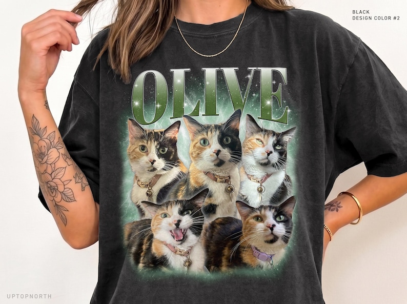 May include: A black t-shirt featuring the word OLIVE in large green letters above a graphic of five calico cats. The cats are shown in various poses, wearing collars with small charms, set against a soft green glowing background.
