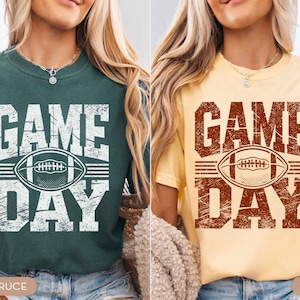 May include: Two t-shirts, one teal and one yellow, featuring a distressed "GAME DAY" design and a football graphic. These short-sleeved shirts are ideal for casual wear, suitable for football enthusiasts.