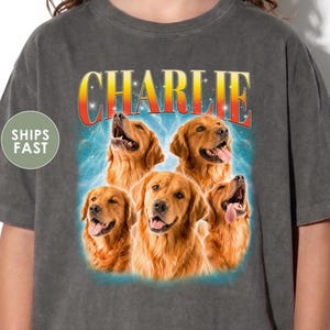 May include: A charcoal gray t-shirt featuring a graphic print of five golden retriever dogs arranged in a cluster. Above the dogs, the name CHARLIE is printed in a bold, yellow-to-red gradient font against a blue, lightning-like background.