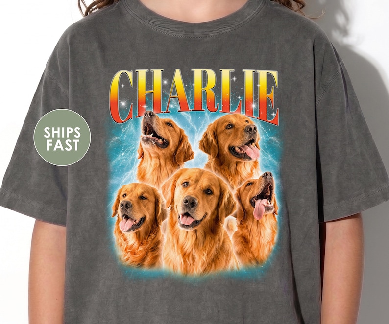 May include: A charcoal gray t-shirt featuring a graphic print of five golden retriever dogs arranged in a cluster. Above the dogs, the name CHARLIE is printed in a bold, yellow-to-red gradient font against a blue, lightning-like background.