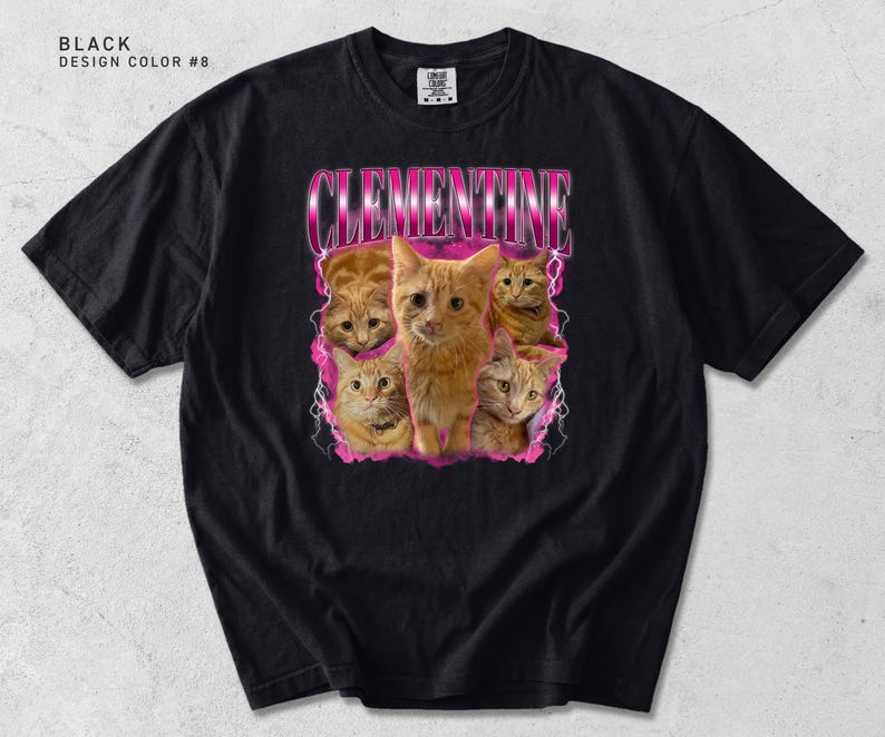 Pu&ograve; includere: T-shirt nero con una grafica di gatti tabby arancioni e il nome "CLEMENTINE" in un font rosa retr&ograve;. La maglietta ha un girocollo e maniche corte. Il testo "BLACK DESIGN COLOR #8" &egrave; in alto a sinistra.
