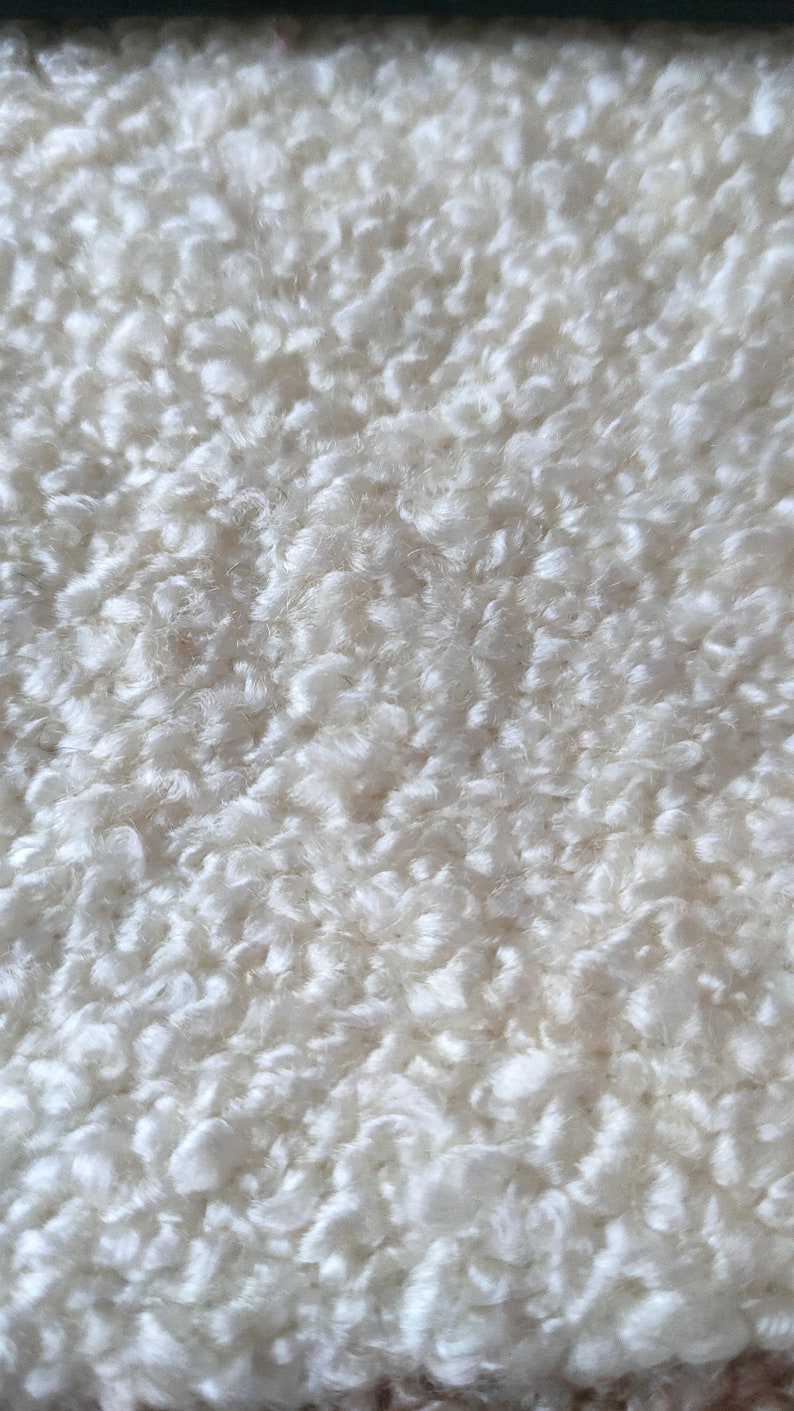 K&ouml;nnte beinhalten: Nahaufnahme eines wei&szlig;en, strukturierten Stoffes mit einem geschlungenen, zotteligen Aussehen. Das Material hat eine weiche, wolkenartige Textur mit unterschiedlichen Tiefen und Dichten. Der Gesamteffekt ist eine flauschige, einladende Oberfl&auml;che.