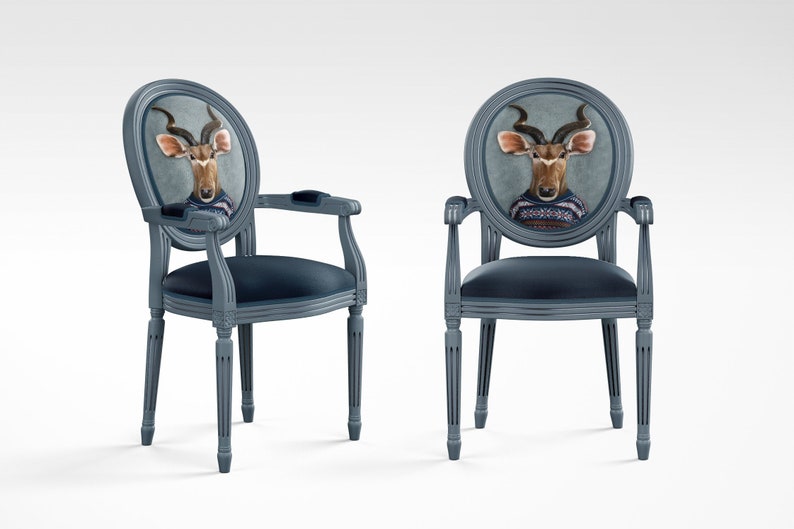May include: Two gray chairs with oval backs featuring a printed image of a kudu antelope wearing a sweater. The chairs have a dark blue velvet seat and are made of wood.