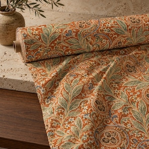May include: A roll of fabric featuring a repeating pattern of sage green leaves, small white flowers, and circular motifs with brown centres set against a vibrant burnt orange background. The textile displays a dense, intricate botanical design.