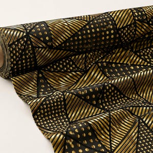 Pu&ograve; includere: Un rotolo di tessuto con un motivo geometrico di triangoli neri e oro metallizzato. Il design alterna sezioni a righe dorate diagonali e sezioni a pois dorati su sfondo nero, avvolto attorno a un supporto cilindrico in cartone.