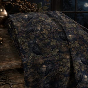 May include: A folded piece of dark navy blue fabric featuring a repeating pattern of black ravens perched among green foliage, berry clusters, and stone urns under a full moon. The textile displays a detailed, dark, and atmospheric print.