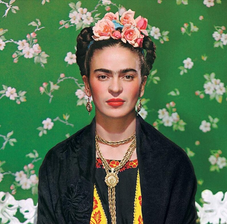 May include: Portrait of a woman with dark hair, wearing a floral crown, gold jewelry, and a black shawl. The background is a green floral pattern. The woman has a serious expression and red lipstick.