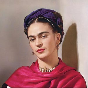 May include: A portrait of a person wearing a purple head wrap, a red shawl, and gold hoop earrings. The person is also wearing a necklace with a white and gold design. The background is a neutral color.