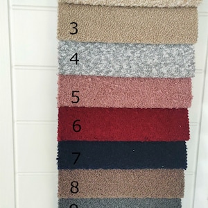 K&ouml;nnte beinhalten: Elf Stoffmuster in verschiedenen Farben werden vertikal angeordnet. Die Muster sind nummeriert. Die Farben umfassen Creme, Beige, Braun, Grau, Rosa, Rot, Marineblau und Dunkelgr&uuml;n. Der Stoff hat eine strukturierte, geschlungene Optik.