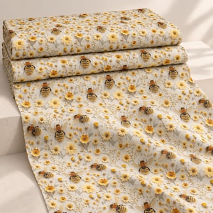 May include: A folded bolt of off-white fabric featuring a repeating pattern of yellow flowers, green stems, and brown and yellow bumblebees. The textile displays a dense, scattered arrangement of botanical elements and insects across the surface.
