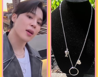 May include: A silver necklace with a heart charm that says "Nice" and a charm of angel wings. The necklace is on a black display stand.