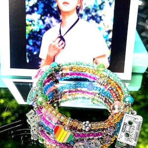 May include: Multi-strand bracelet with colorful beads, charms, and a rainbow heart charm. The bracelet also features a charm that says "Music is my muse" and a cassette tape charm.