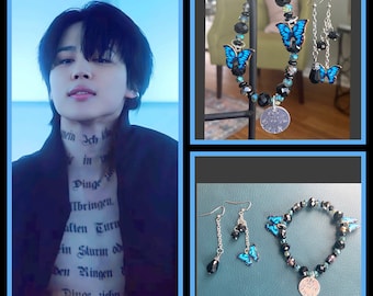 May include: A jewelry set featuring a bracelet and earrings with blue butterfly charms and black beads. The bracelet and earrings have a silver-colored charm with the inscription "Love me Jimin". The image also includes a person with text on their neck and chest.