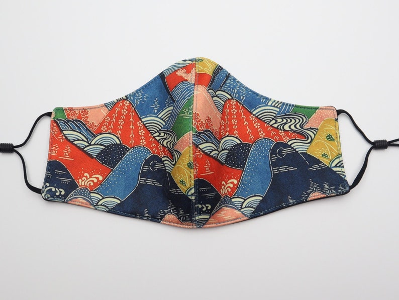May include: A reusable face mask with a colorful Japanese-inspired mountain and wave pattern. The mask is made of fabric and has adjustable ear loops.
