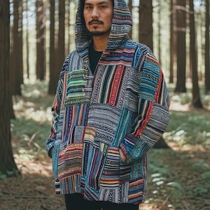 May include: A multi-coloured patchwork hooded jacket with a button closure and pockets. The jacket features a variety of patterns and is worn in a forest setting. The colours include blue, red, green, and grey.