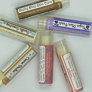 May include: Six different flavored lip balms in clear tubes with colorful labels. The labels have snowflakes and text that reads "Safety Seal", "Handmade All Natural Lip Balm", "Vanilla Snowdrop", "Creme Brulee", "Sugar Plum Punch", and "Bipity Bliss Skin Care".