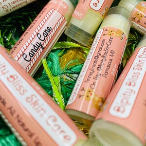 May include: A collection of pink and white lip balm tubes with a reindeer design and the text "Ripity Bliss Skin Care". The lip balms are labeled with different flavors, including "Candy Cane" and "Soybean Oil Essential Oil & Flavor Oil".