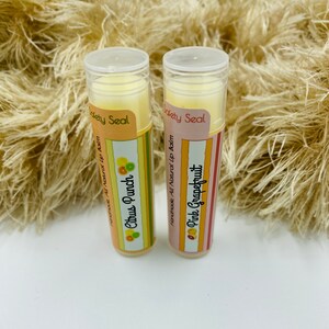 May include: Two tubes of lip balm with colorful labels. The lip balm on the left is labeled "Citrus Punch" and the lip balm on the right is labeled "Pink Grapefruit". Both tubes have a yellow and white striped label with the words "Handmade, All Natural Lip Balm" and "Safety Seal".