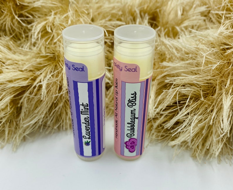May include: Two lip balm tubes with purple and white labels. The labels say "Homemade All Natural Lip Balm" and "Safety Seal". The lip balm flavors are "Lavender Mint" and "Bubbleseum Bliss".