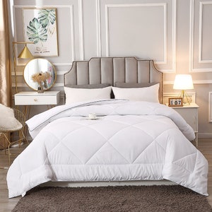 May include: White down comforter with a diamond stitch pattern on a bed with a gray headboard. The comforter is folded back to show the white sheets underneath.