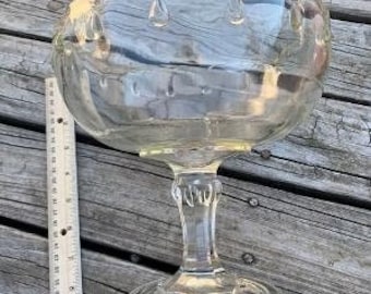 May include: A clear glass pedestal bowl with a scalloped edge and a fluted base. The bowl is perfect for serving fruit, candy, or other treats.