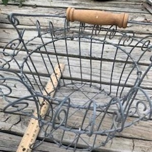 May include: A gray metal wire basket with a wooden handle. The basket has a decorative design and is perfect for storing items.