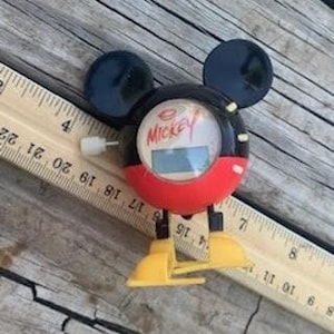 May include: A black and red wind-up Mickey Mouse toy with a digital clock face. The clock face reads "Mickey" and has a digital display.