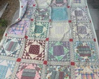 May include: A patchwork quilt with a variety of colors and patterns, including red, blue, green, and white. The quilt is made of squares and rectangles, and the seams are visible. The quilt is laid out on a concrete surface.