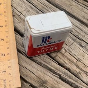 May include: A small, white, rectangular spice tin with a red label. The label says "McCormick" and "Ground Thyme".