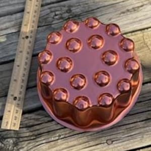 May include: Copper-colored, round cake pan with a fluted edge and a raised, textured surface of small, rounded bumps.
