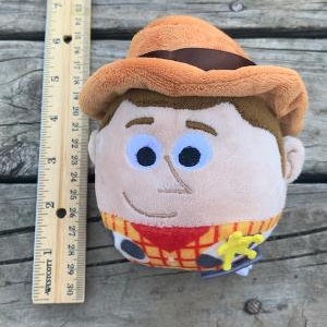 May include: A plush toy of Woody from Toy Story. He is wearing his signature brown cowboy hat, red bandana, and yellow vest. He has a friendly smile and blue eyes.