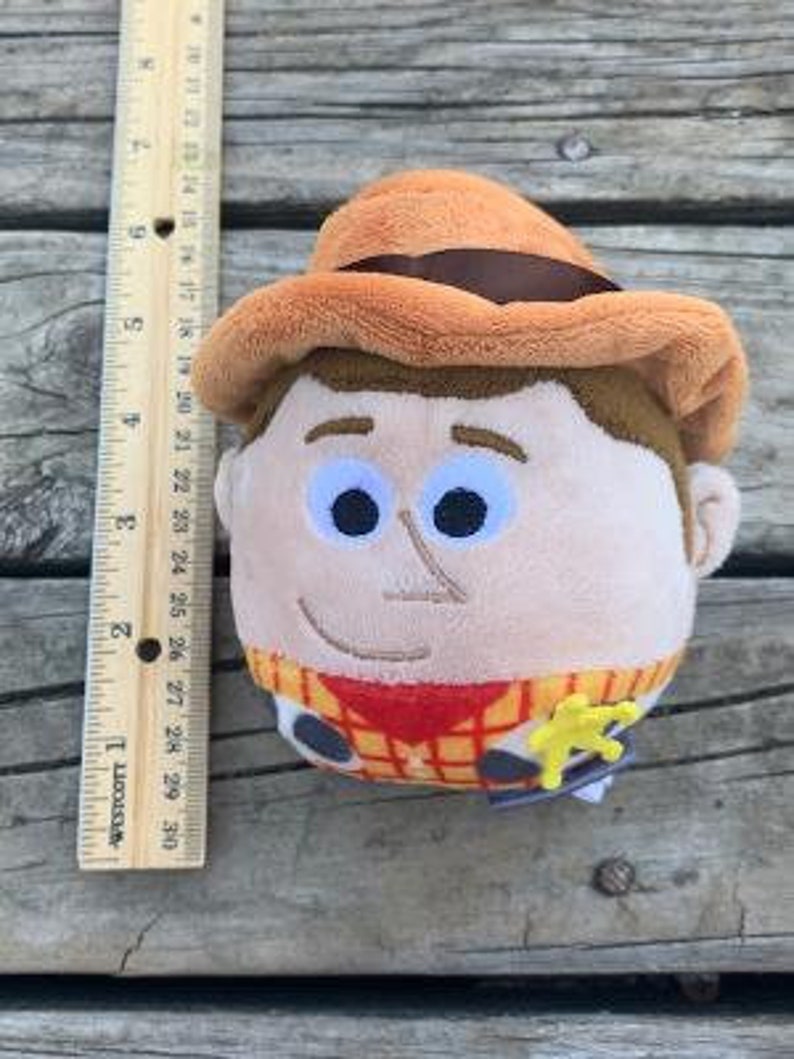 May include: A plush toy of Woody from Toy Story. He is wearing his signature brown cowboy hat, red bandana, and yellow vest. He has a friendly smile and blue eyes.