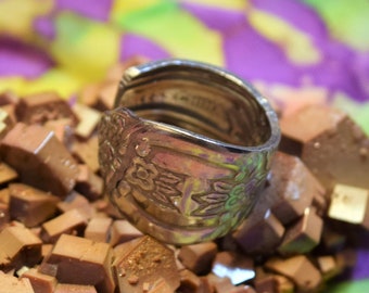 Könnte beinhalten: Ein silberner Ring mit floralem Design, der auf einem Haufen brauner Kristalle liegt.