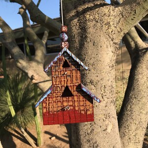 May include: A ceramic birdhouse with a red and brown glaze, hanging from a tree branch. The birdhouse has a small opening for birds to enter and a decorative design on the front.
