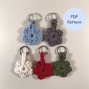 Peut inclure: Cinq porte-clés en forme de fleur crochetés dans différentes couleurs : bleu clair, gris, blanc, rouge et vert. Chaque porte-clés est doté d’un anneau en métal argenté.