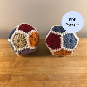 May include: Two crocheted balls with a geometric pattern in shades of red, blue, orange, white, and purple. The balls are on a wooden surface. PDF Pattern.