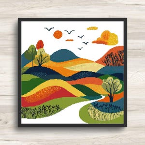 May include: A framed cross-stitch landscape featuring rolling hills in shades of green, orange, yellow, and blue. A white path winds through the scene, with trees, birds, and a sun in the sky. The artwork is displayed in a black frame.
