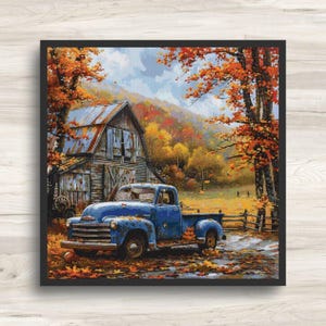 May include: A framed cross-stitch showing an autumnal landscape. A blue pickup truck is parked near a barn, with fallen leaves scattered around. The background includes trees with orange and yellow leaves, and a mountain range.