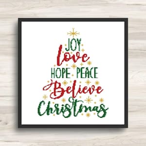 May include: A cross-stitch pattern arranged in a triangular tree shape featuring the words JOY, love, HOPE, PEACE, Believe, and Christmas in red and green thread, accented with small yellow star motifs on a white background within a black frame.