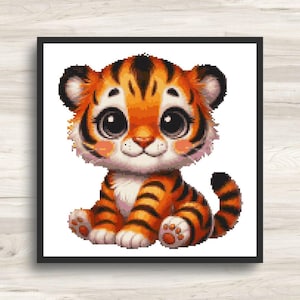 Könnte beinhalten: Ein gerahmtes Kreuzstichbild eines Cartoon-Tigerbabys. Der Tiger hat orange und schwarze Streifen, große Augen und rosa Wangen. Das Kunstwerk ist vor einem weißen Hintergrund platziert und in einem schwarzen Rahmen eingefasst. Der Tiger sitzt.