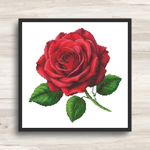 Puede incluir: Un patrón de punto de cruz que muestra una rosa roja grande y vibrante con pétalos superpuestos. La flor está unida a un tallo verde con tres hojas verdes texturizadas y distintas. Todo el diseño se presenta dentro de un marco negro cuadrado.