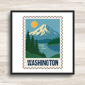 May include: A square cross-stitch pattern framed in black, depicting a postage stamp design of a snow-capped mountain, a yellow sun, and evergreen trees reflected in a lake. The word WASHINGTON is printed in dark blue capital letters at the bottom.